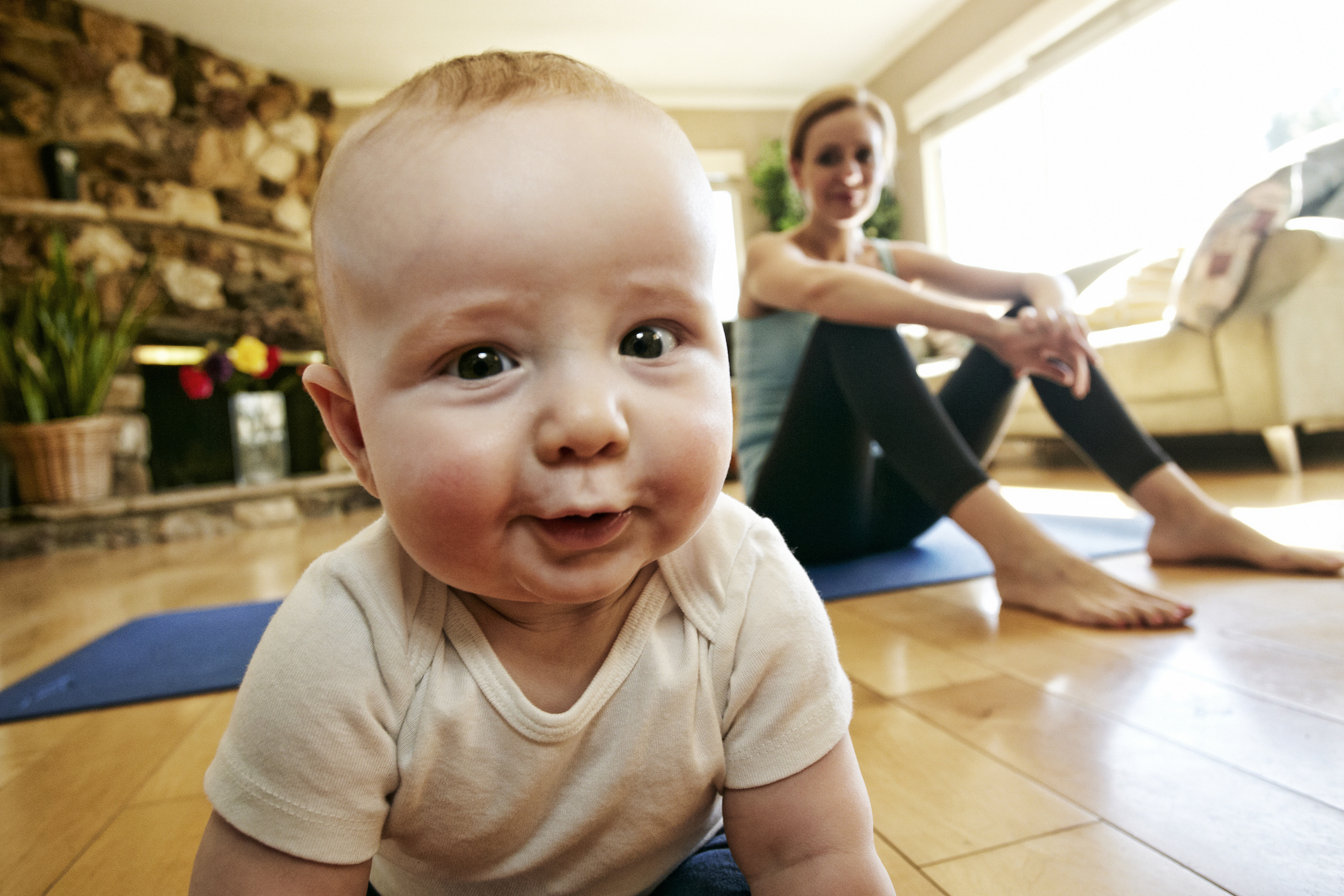 Infant on all fours in foreground with smiling woman seated in background