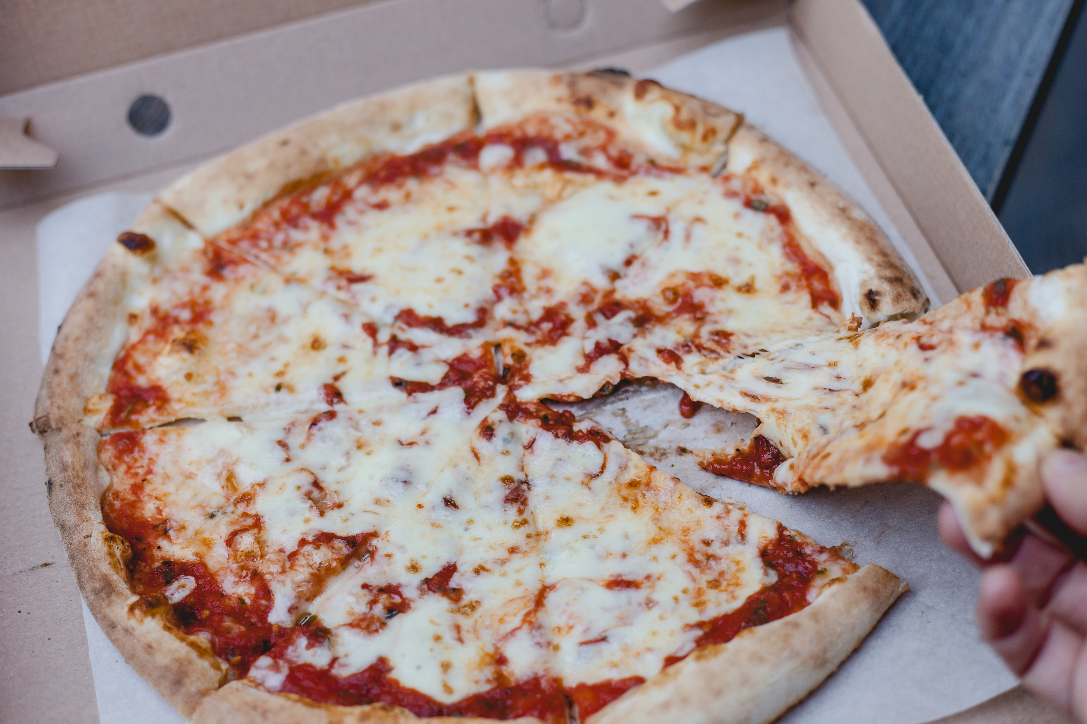 A cheese pizza with one slice partly removed, with hand holding the slice