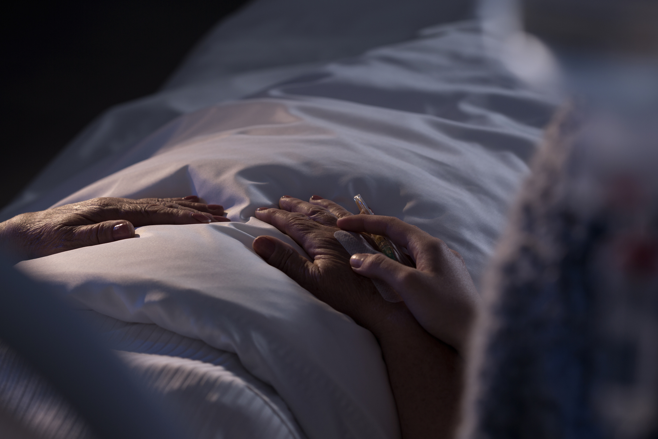 Person resting in bed with another&#x27;s hand holding theirs in comfort