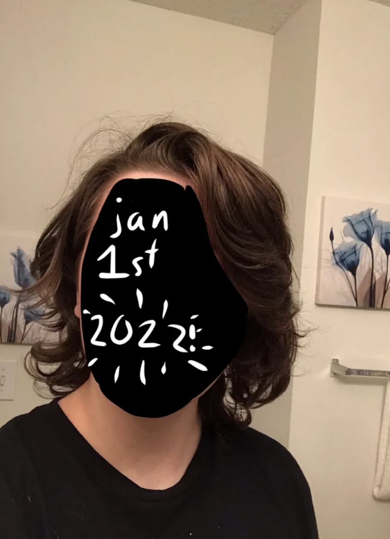 Person with shoulder-length wavy hair in a room, text on face covering features reads &quot;Jan 1st 2022&quot;