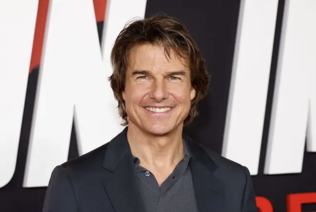 Tom Cruise at an event, wearing a smart casual dark jacket and shirt, smiling for the camera