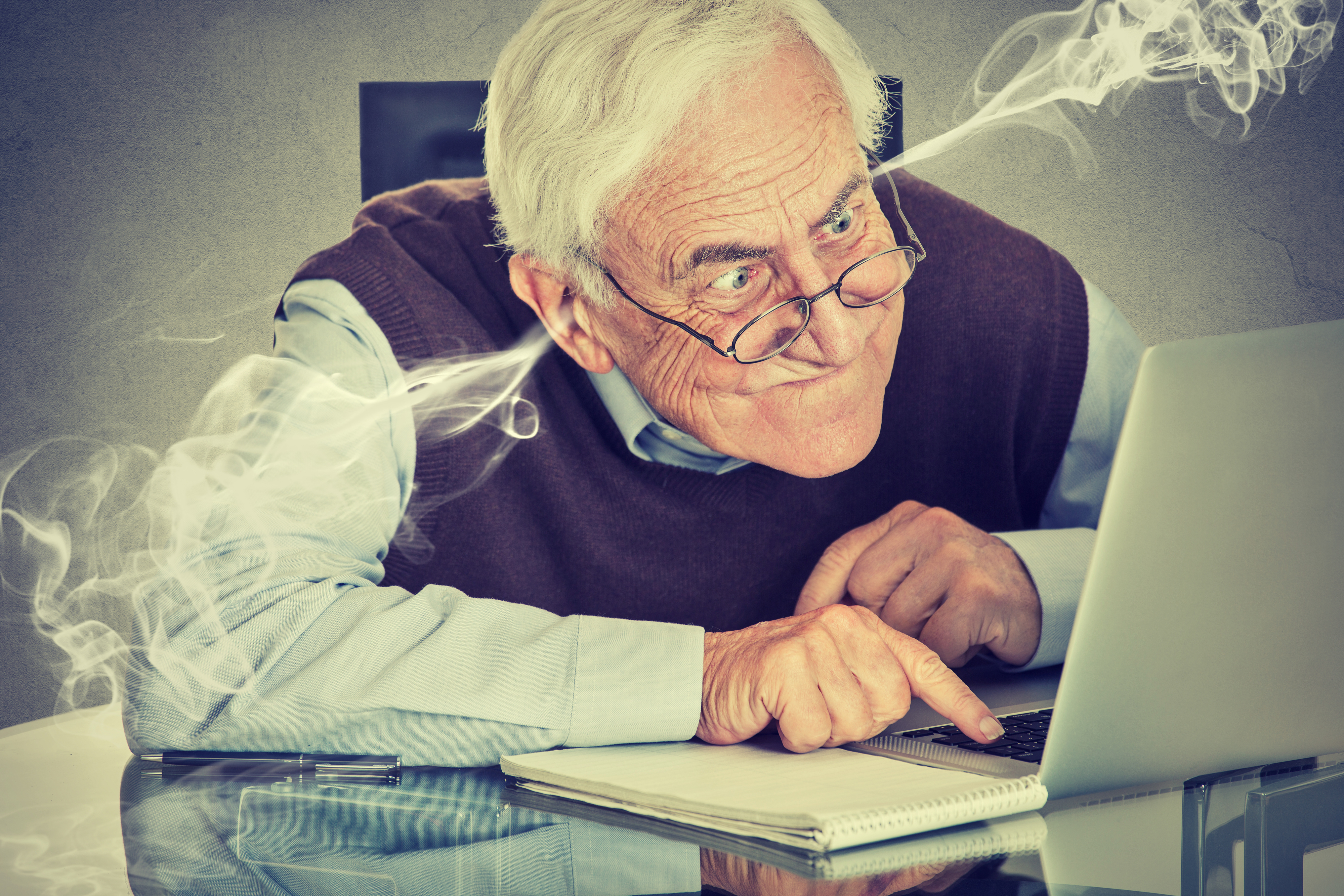 Elderly man intensely looking at a laptop screen with steam coming out of his ears, possibly representing frustration or confusion