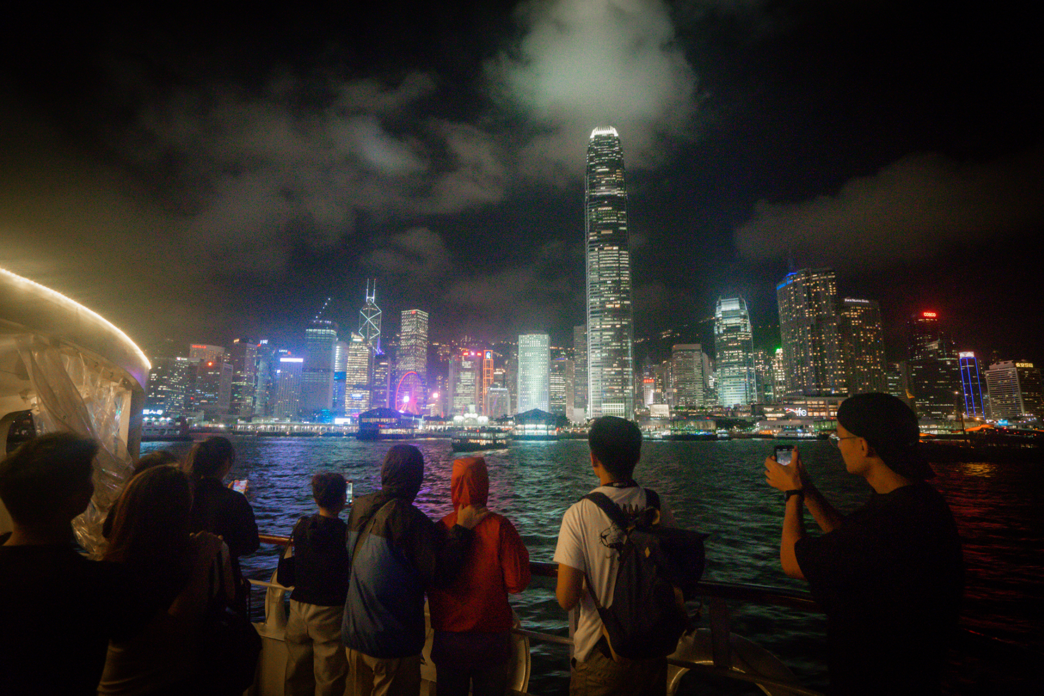 People on a boat viewing a city skyline at night, with illuminated buildings