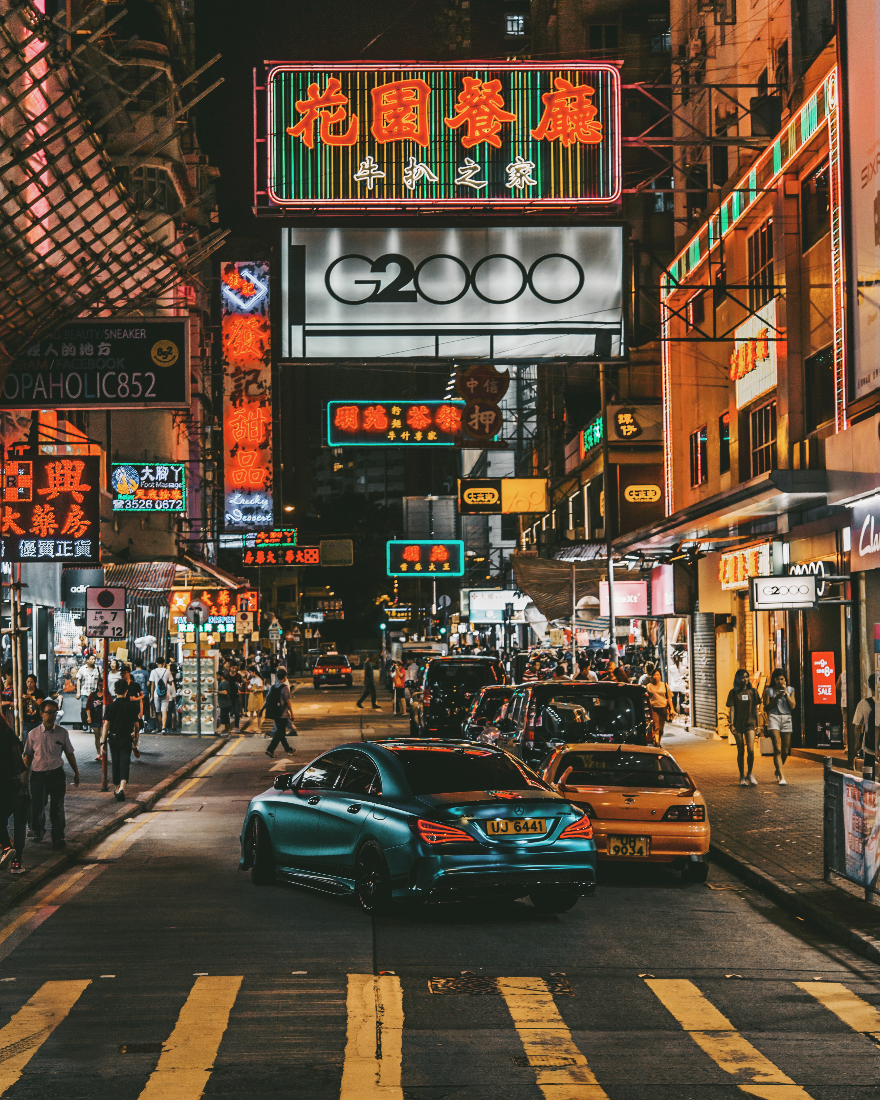 Illuminated street signs at night in a bustling city with pedestrians and cars
