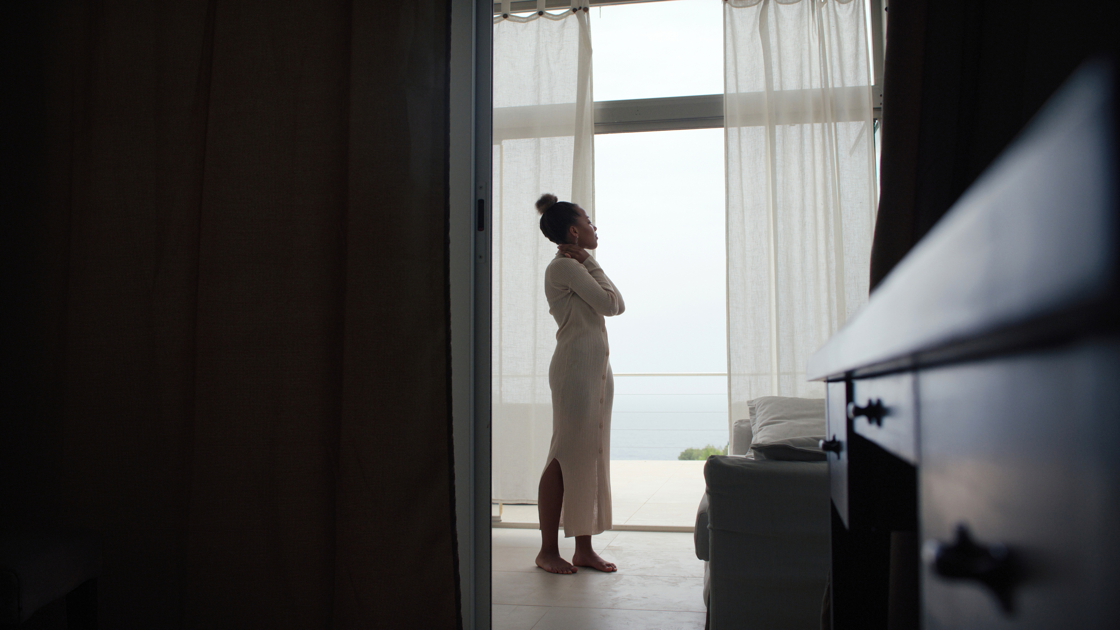 Woman in a robe looking out a window, with a serene expression