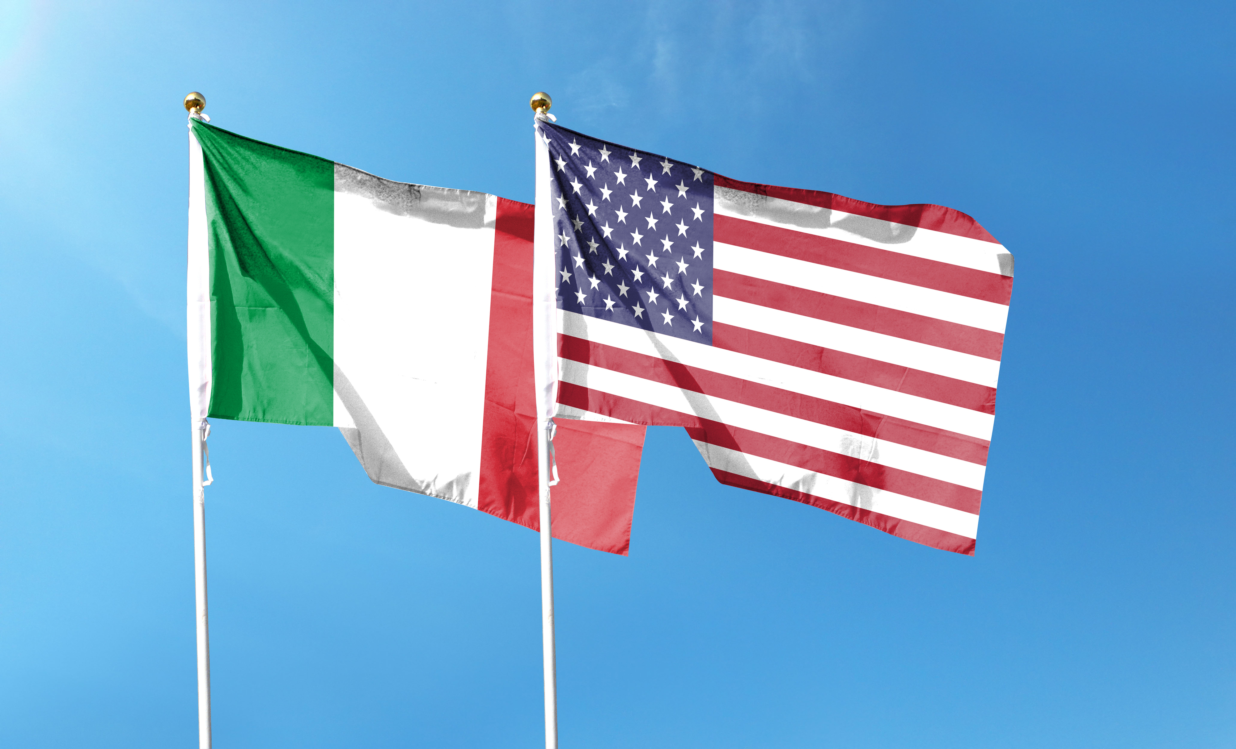 Italian and American flags side by side on poles against a clear sky