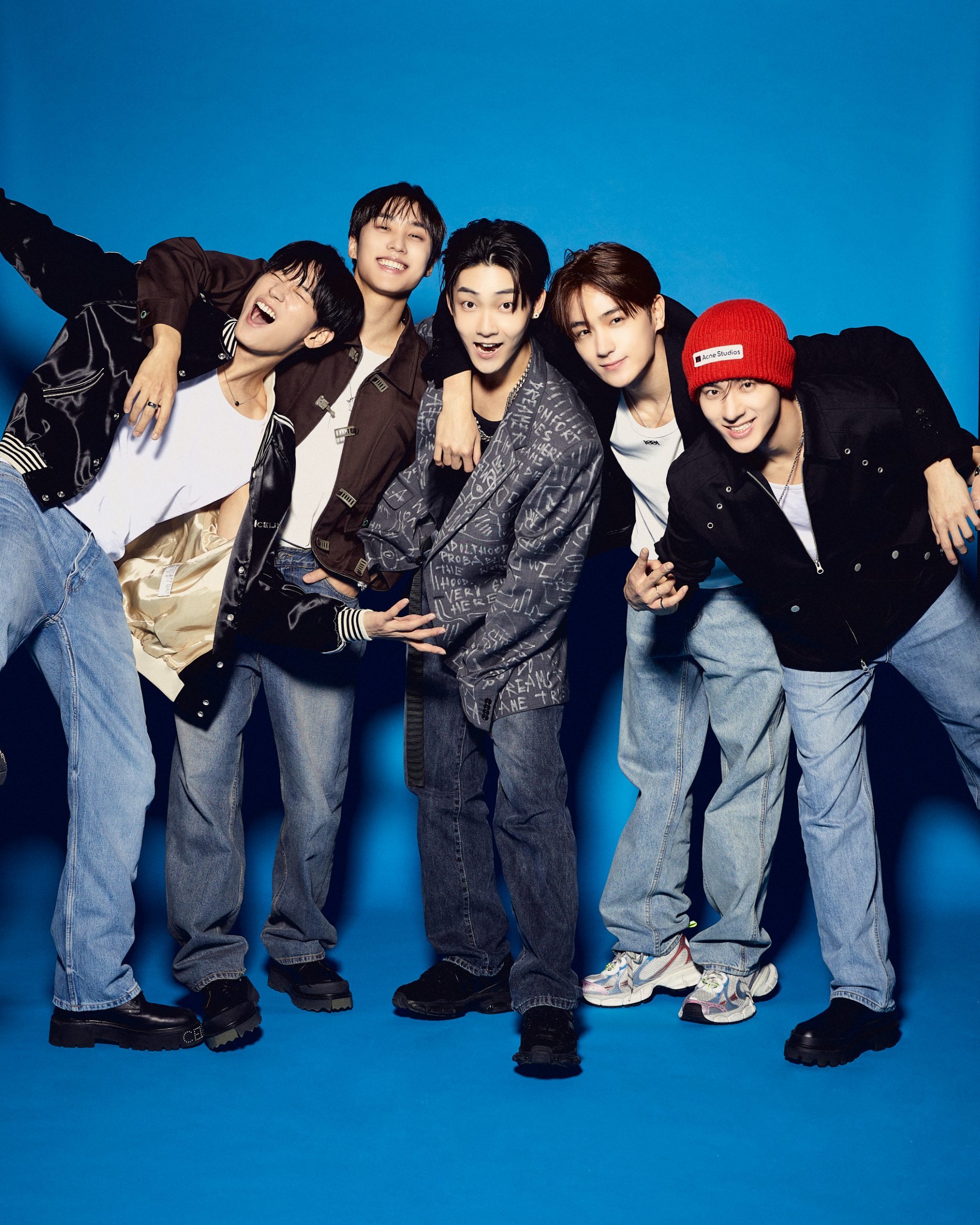 Five members of The Boyz posing playfully, dressed in casual and stylish outfits against a plain backdrop