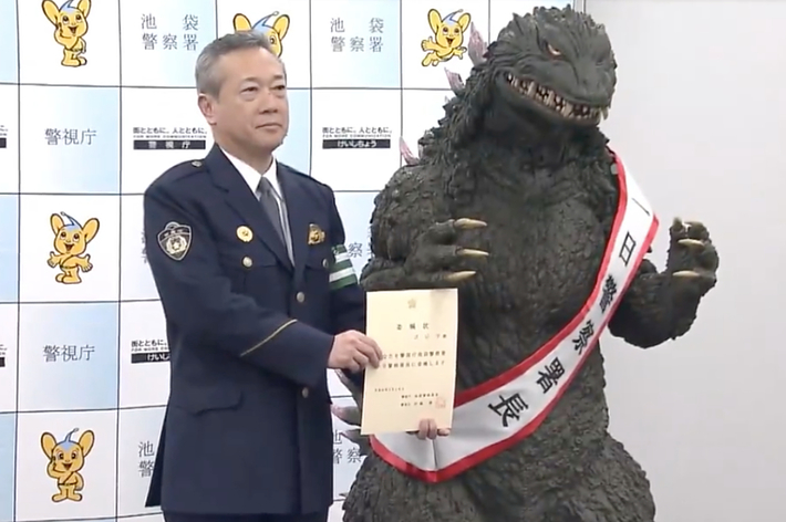 A person in uniform stands next to a person in a Godzilla costume at an event