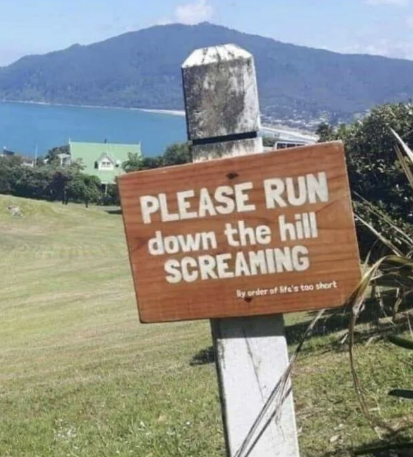 Sign reads &quot;PLEASE RUN down the hill SCREAMING&quot; with &quot;By order of life&#x27;s too short&quot; below, near a hill