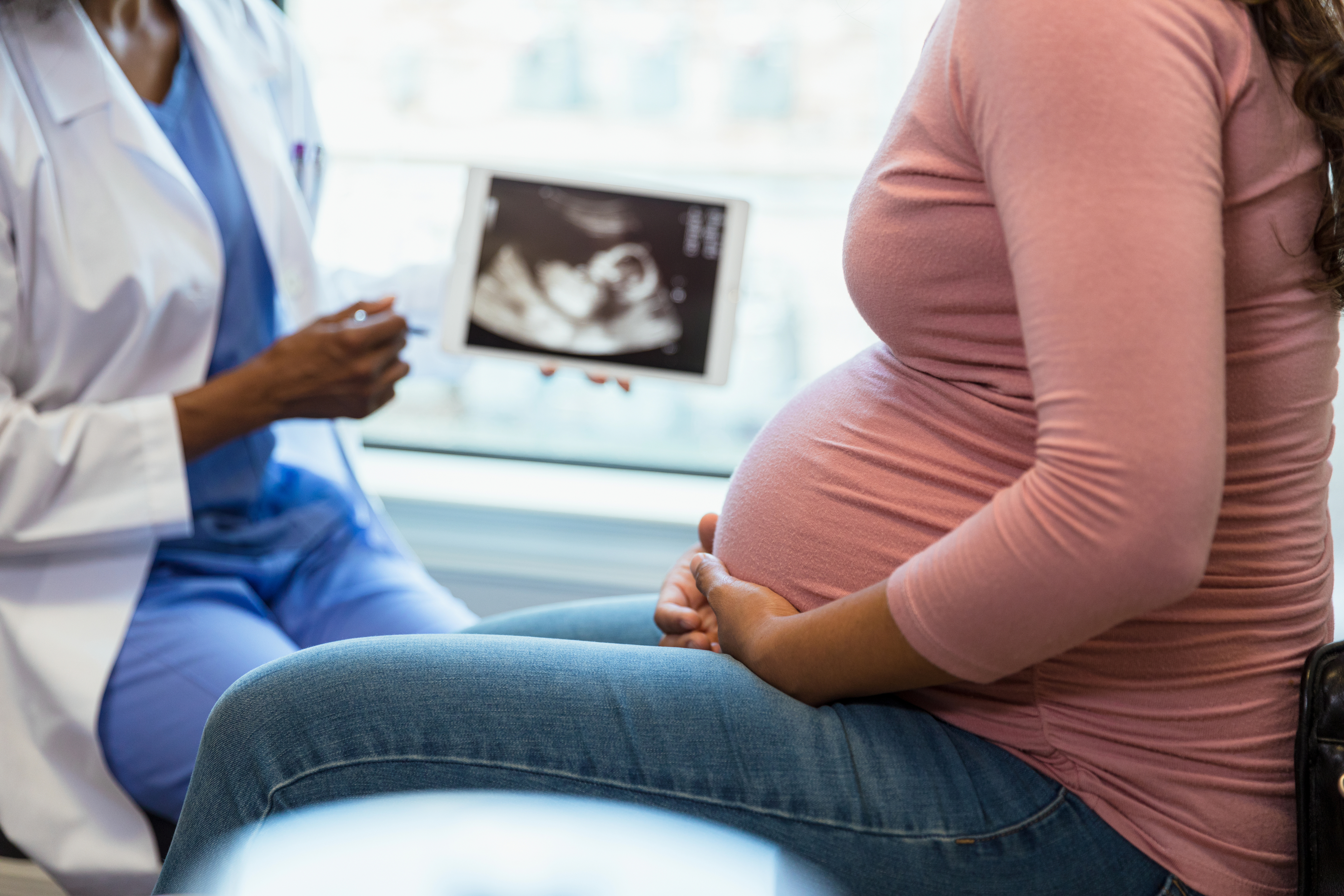 Pregnant person at a medical check-up with a doctor displaying an ultrasound image