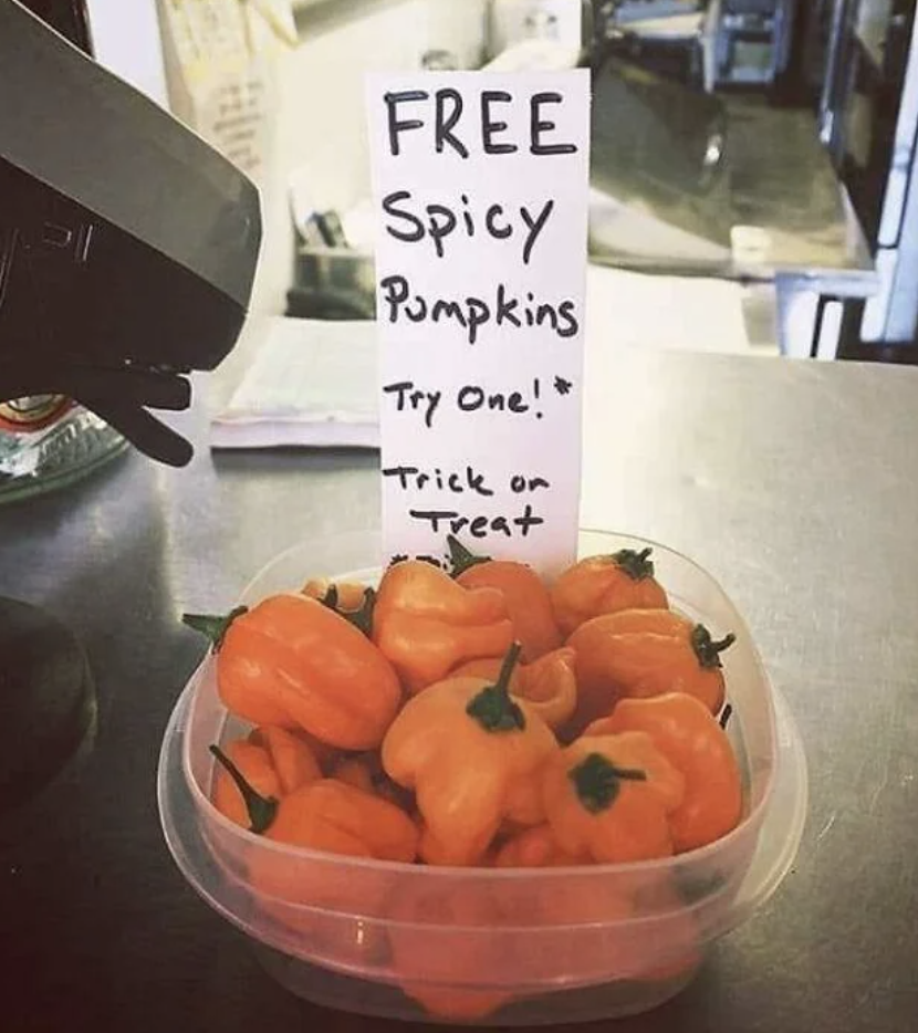 Sign reads &quot;FREE Spicy Pumpkins Try One! Trick or Treat&quot; with a bowl of small orange peppers shaped like pumpkins