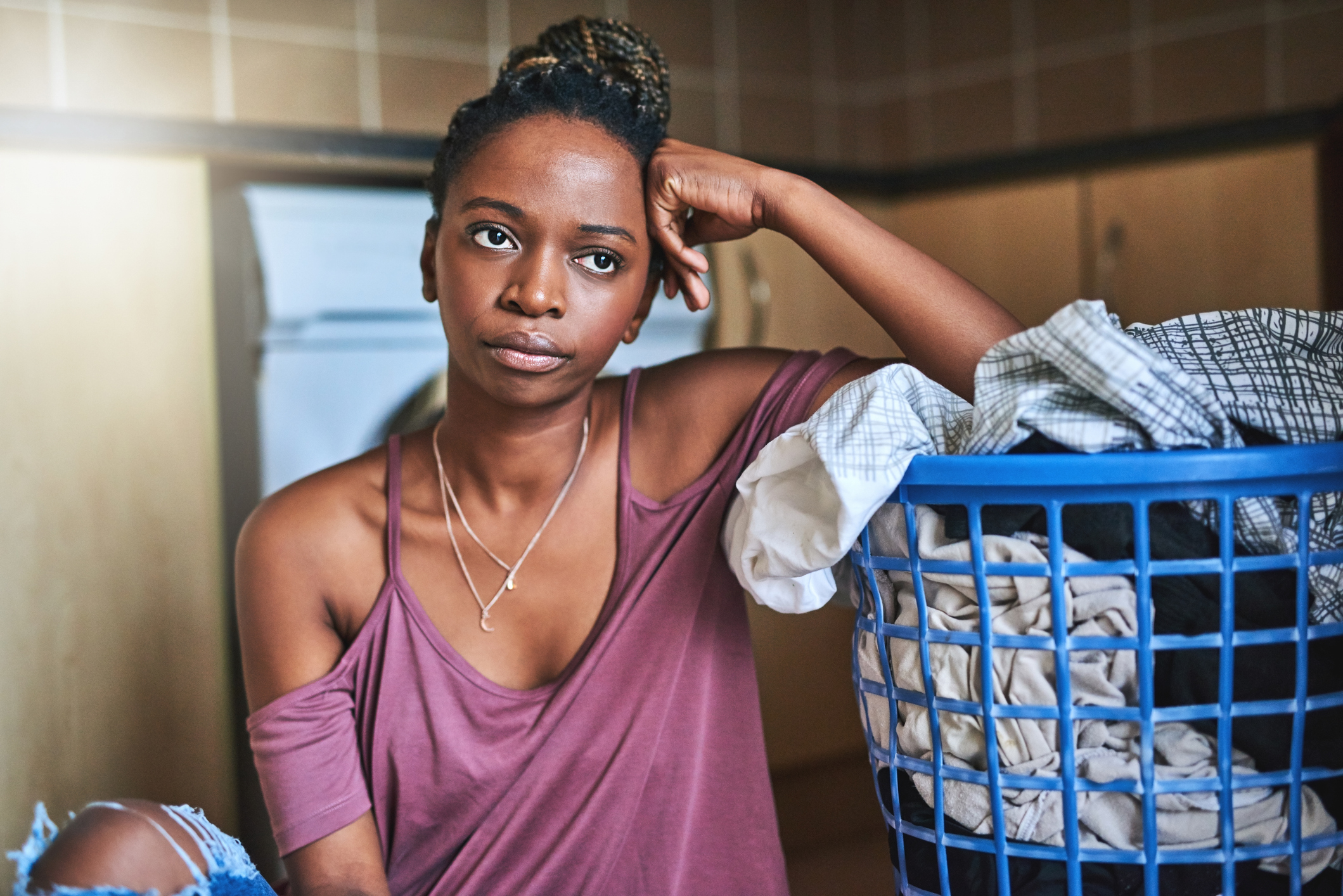 Woman looking tired standing next to a laundry basket, possibly reflecting on relationship dynamics