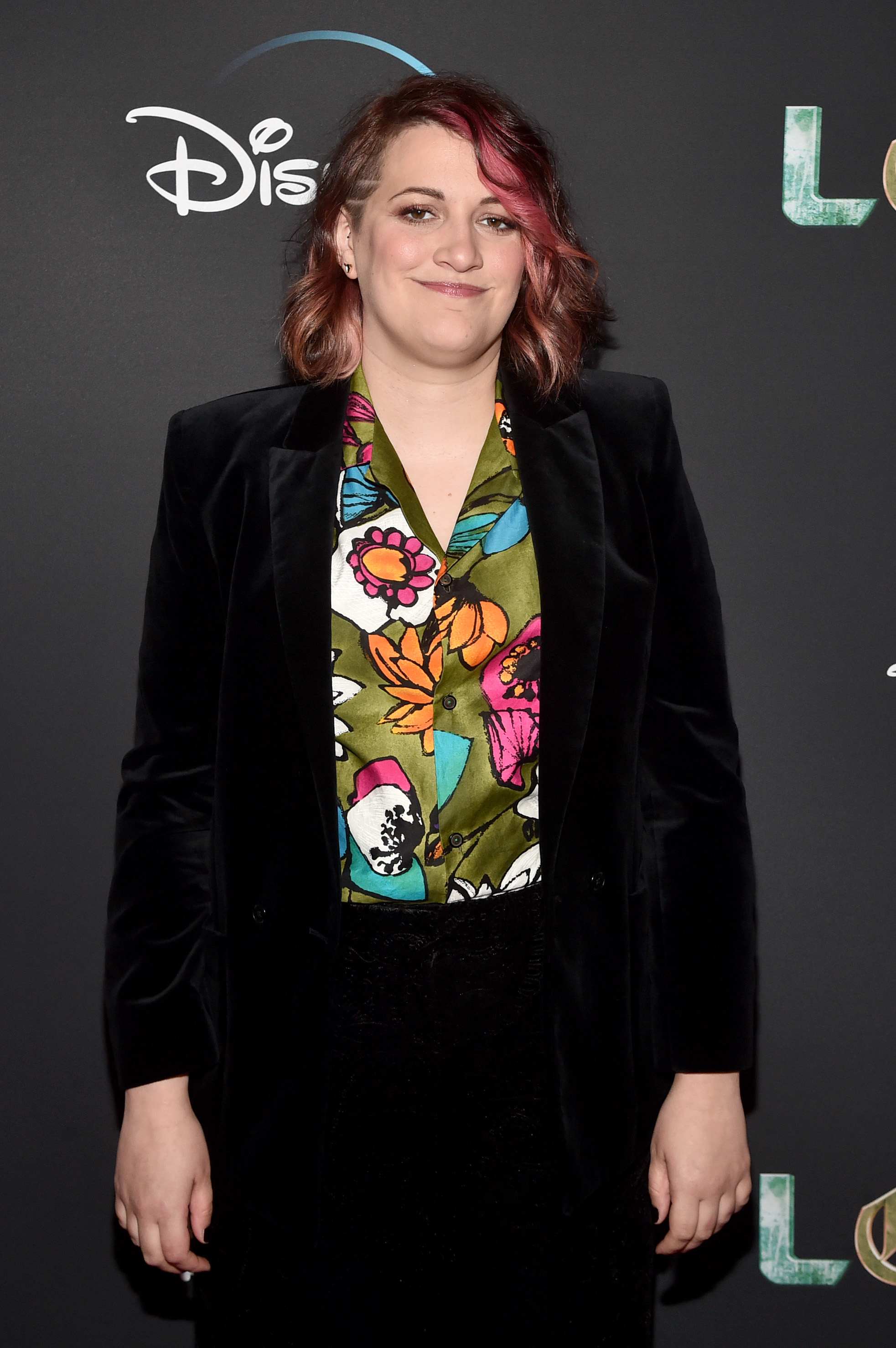 Kate Herron at an event wearing a floral blouse and a blazer