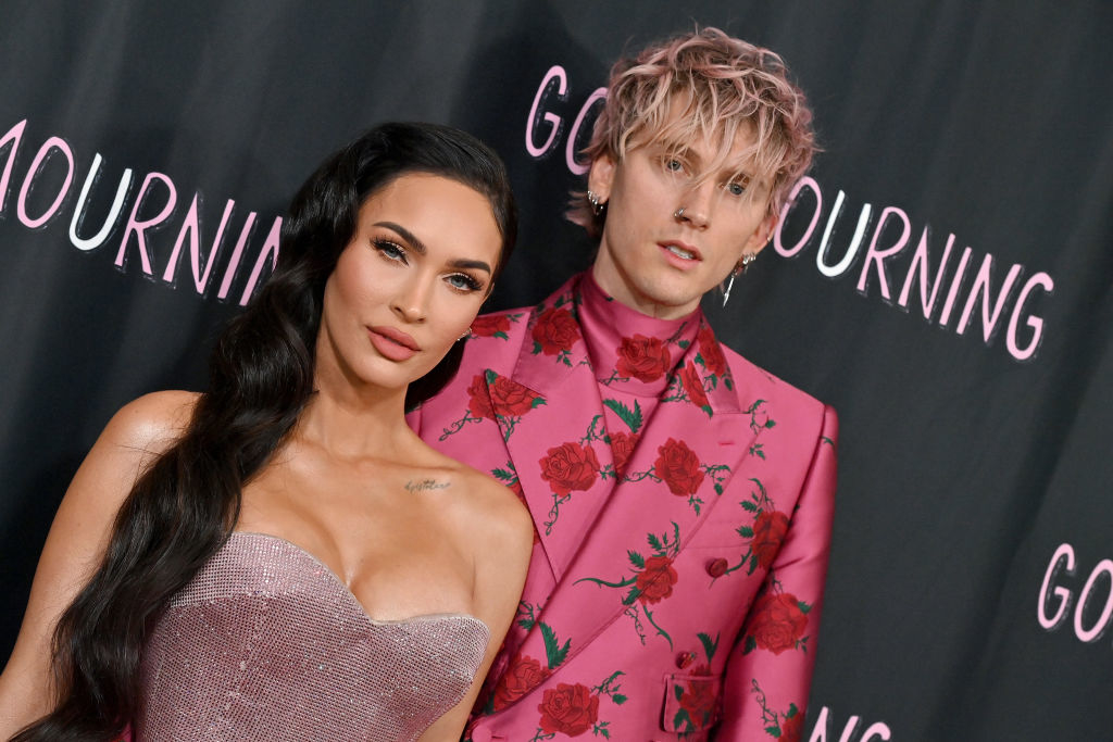 Megan in a strapless glittery gown, standing with Machine Gun Kelly wearing a floral suit, both posing on a red carpet