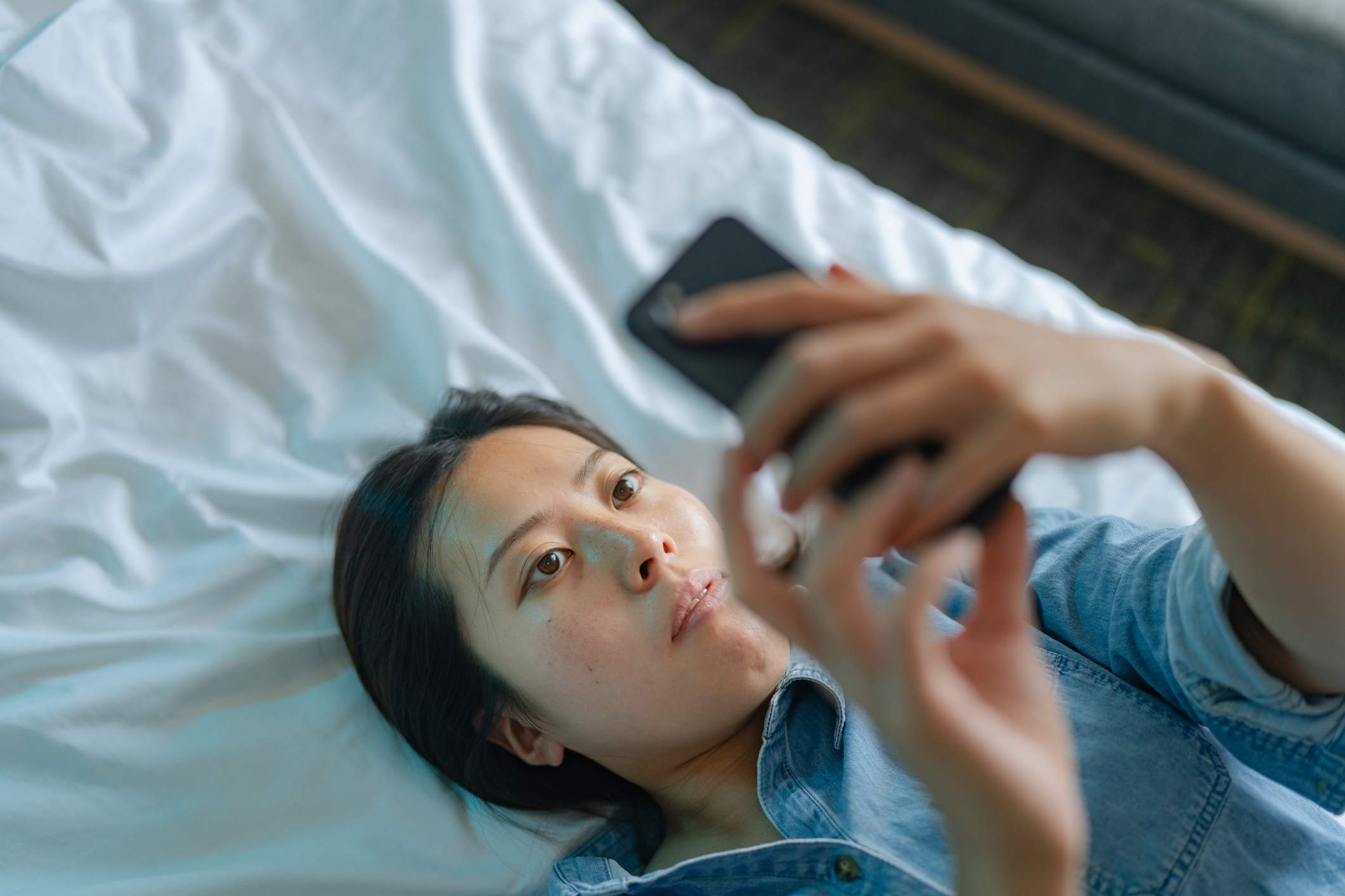 Woman lying on bed looking at phone screen