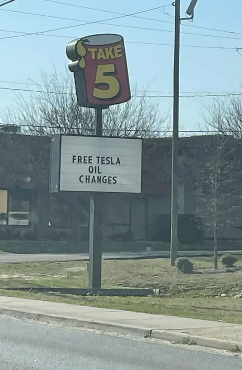 Sign reads &quot;FREE TESLA OIL CHANGES&quot; at a TAKE 5 location, humorously offering a service Teslas do not need