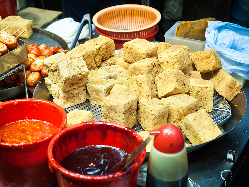 Assorted tofu blocks on a market stall with sauces in buckets nearby