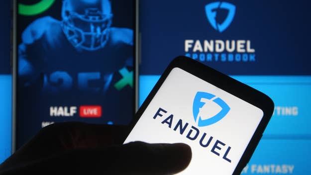 Hand holding smartphone with FanDuel logo on screen, sports betting ads in background