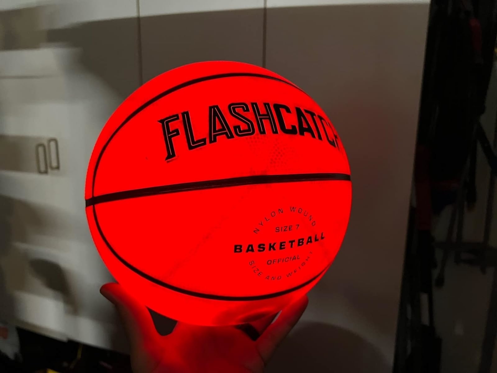 A hand holds up a FLASHCATCH basketball — it glows a bright red orange