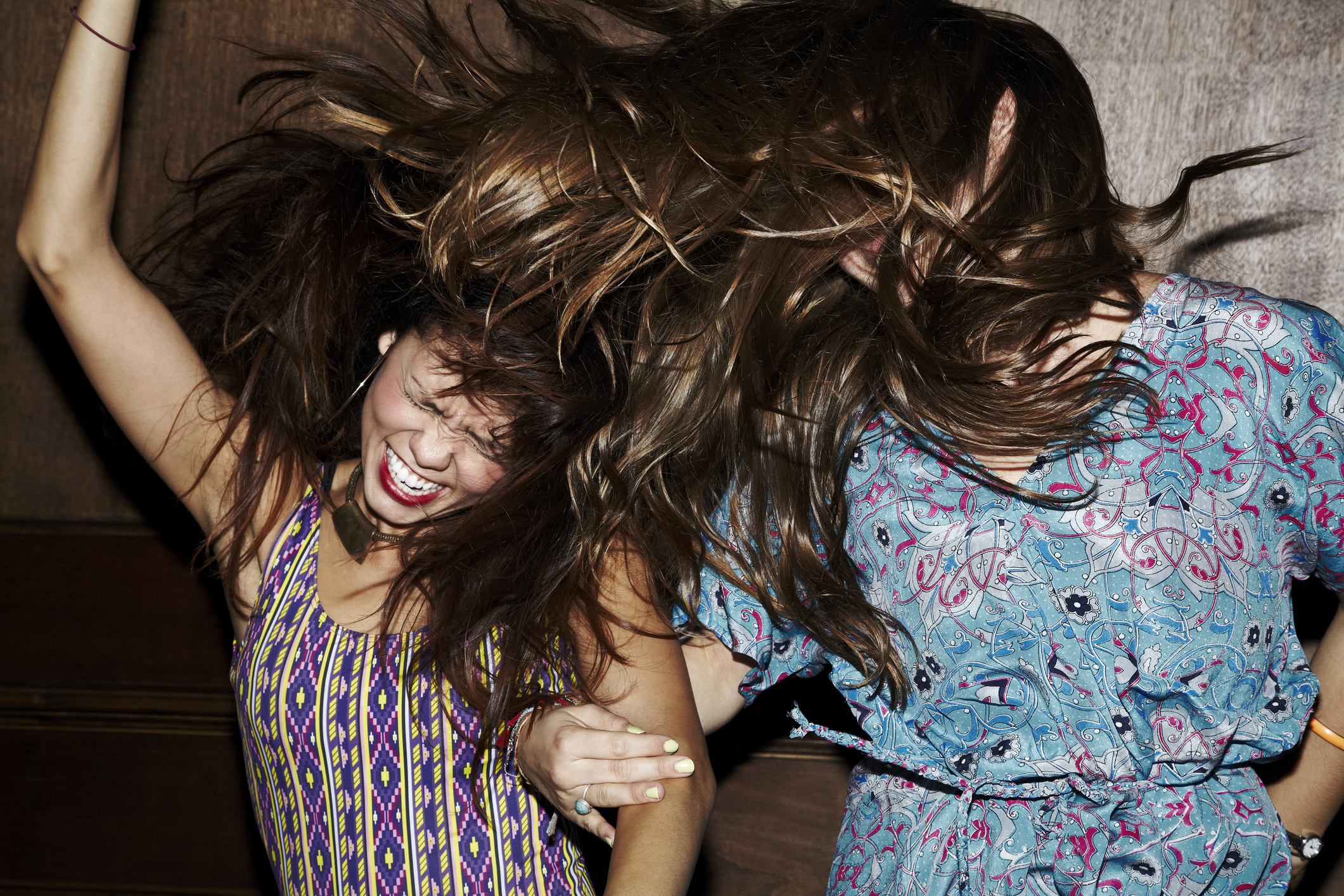 Two people in patterned dresses laughing with hair flipping in the air