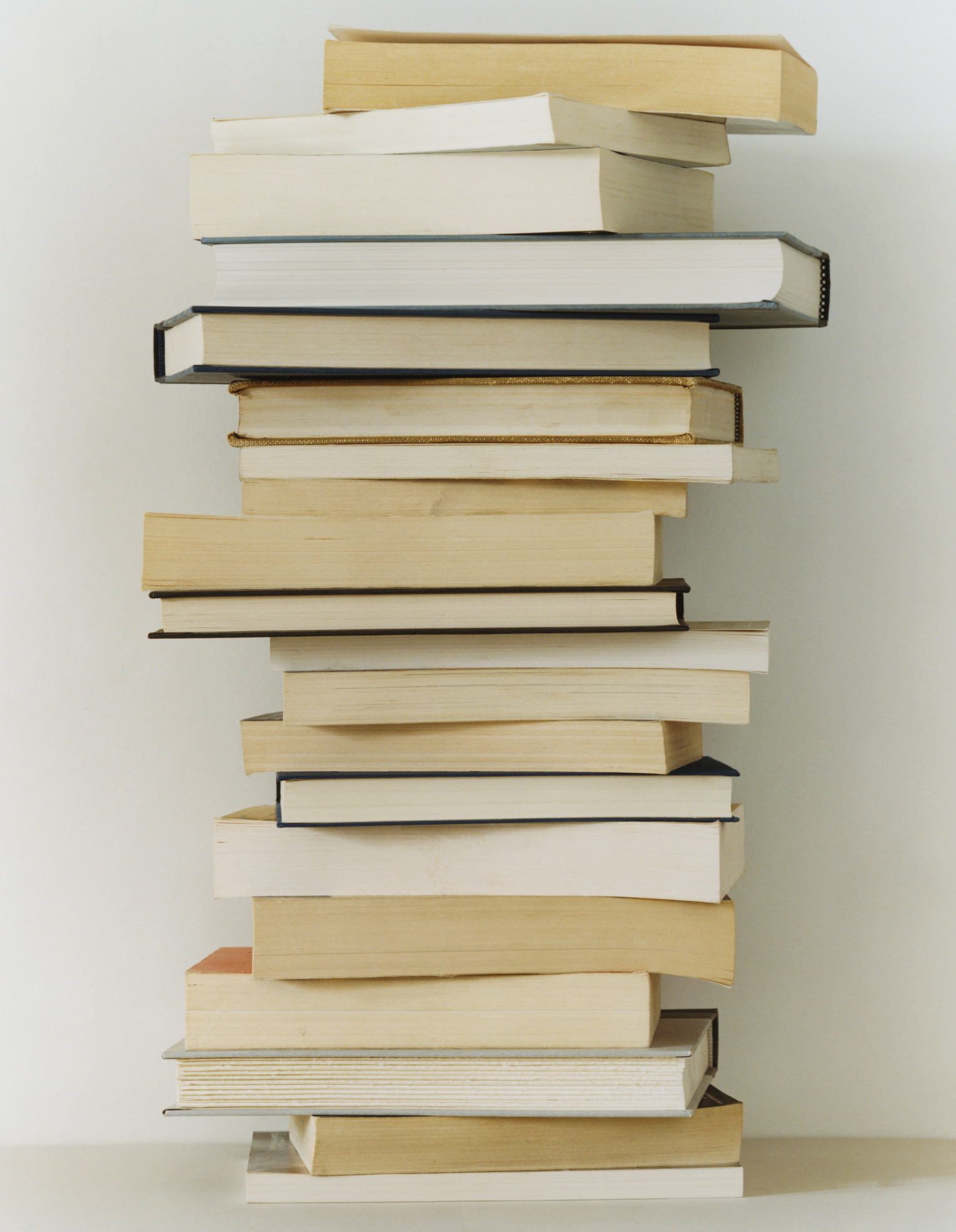 A tall stack of various hardcover and paperback books against a light background