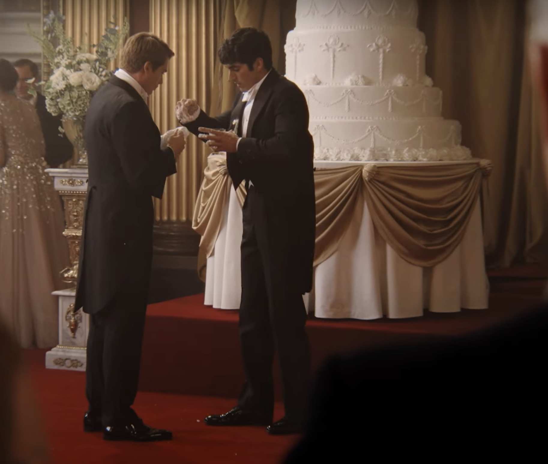 Two men in formal attire exchanging rings in front of a wedding cake