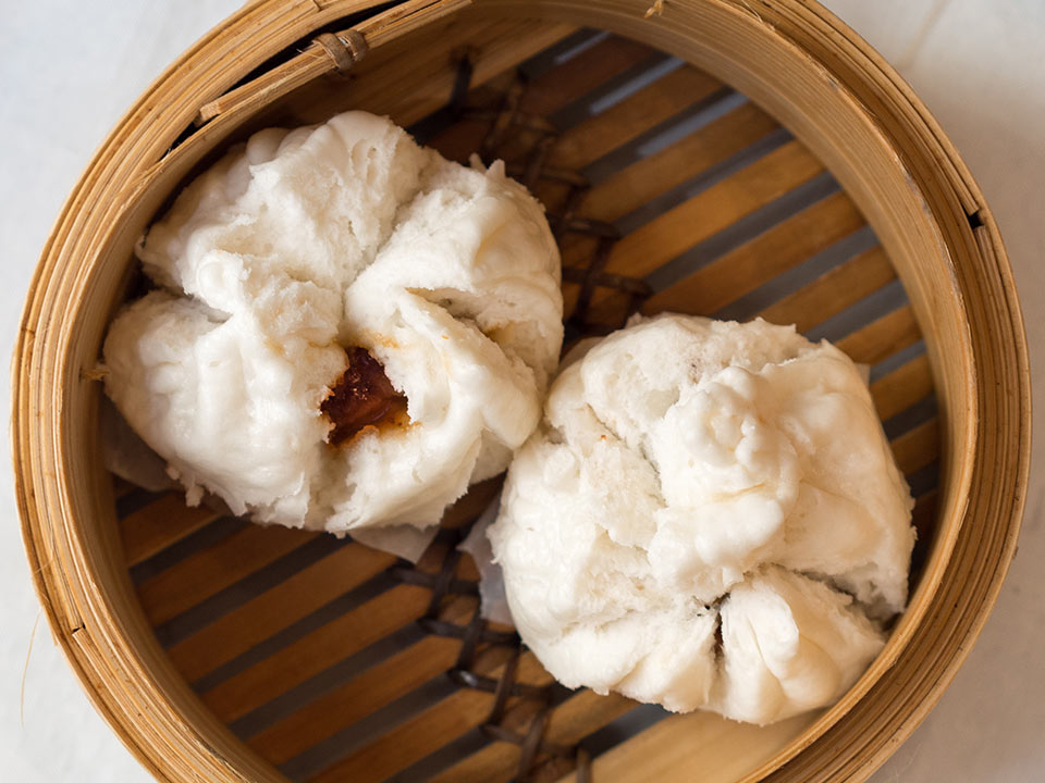 Two steamed buns with visible filling, in a bamboo steamer