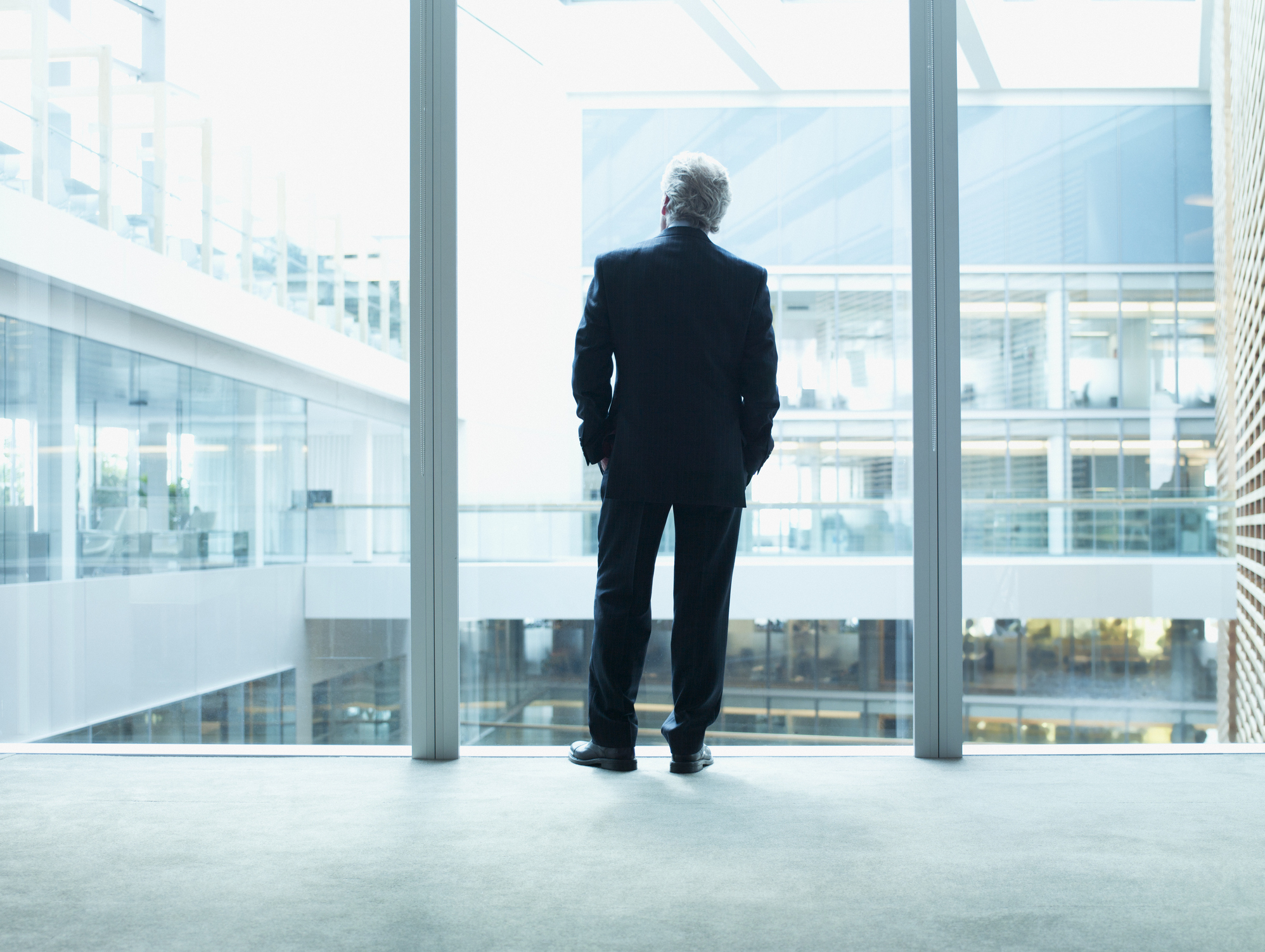 Person in business attire viewed from behind looking out of a large window in an office building