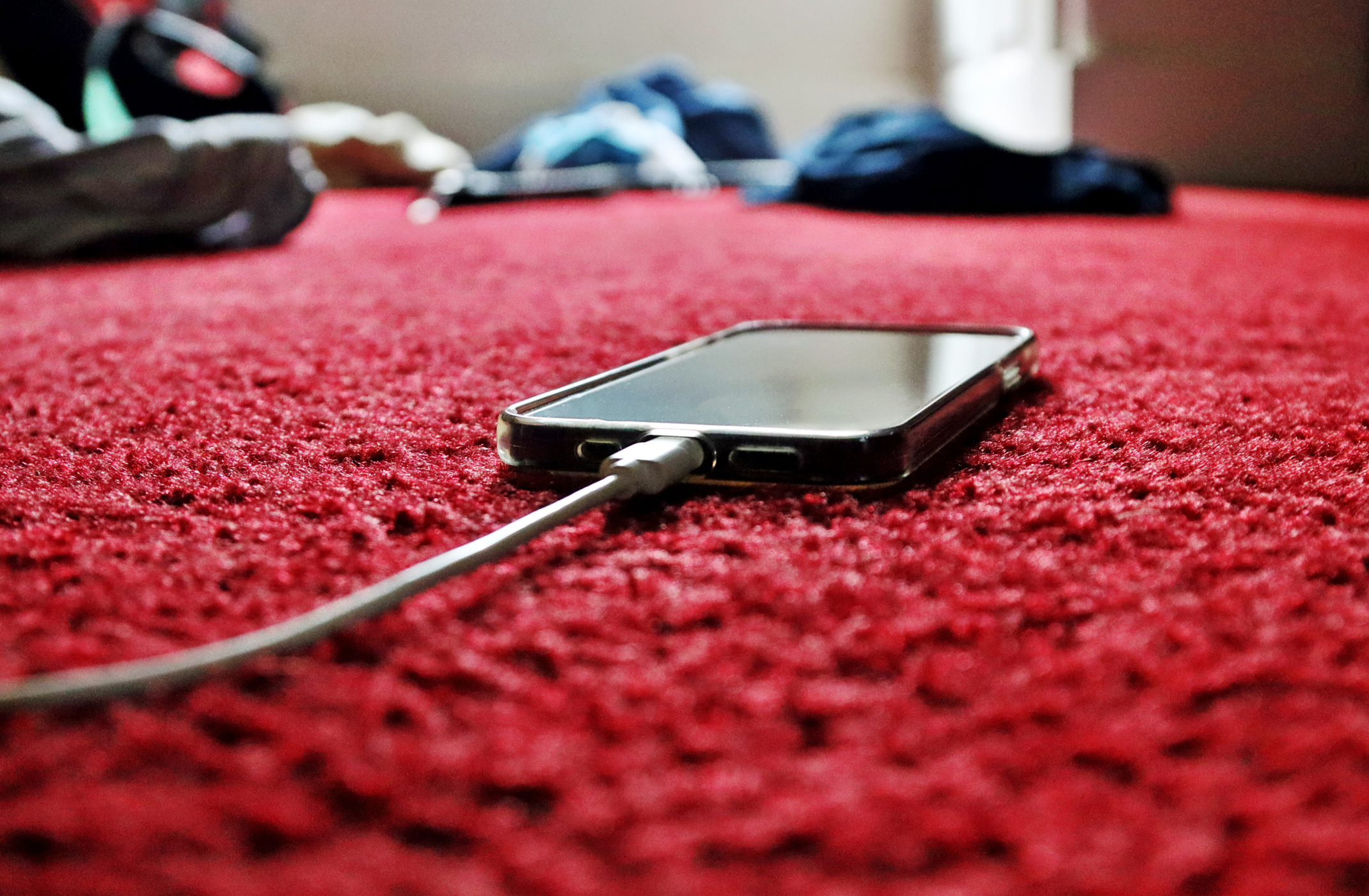 Smartphone charging on a red carpet with clothing items in the background