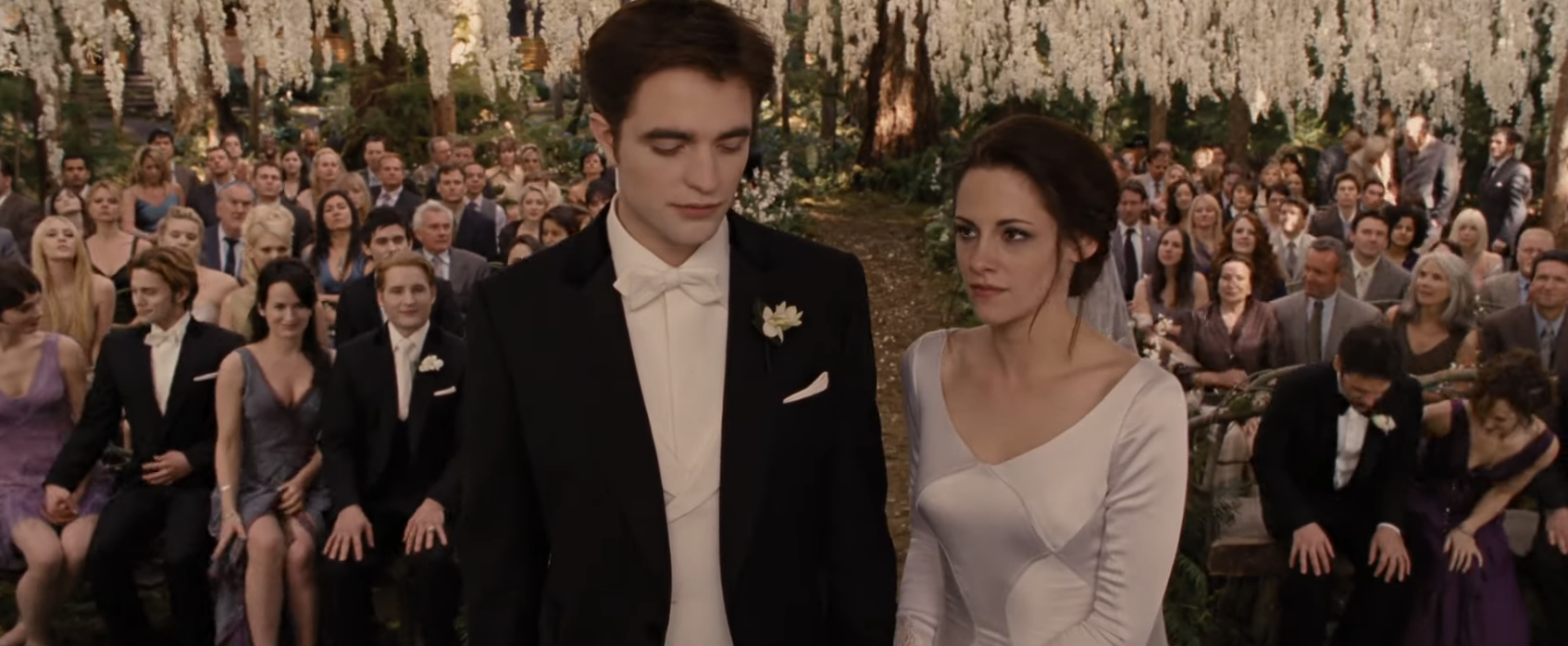 Edward and Bella in formal wedding attire at their outdoor wedding ceremony with guests in the background