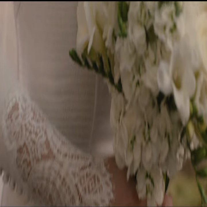 Close-up of a person in a lace-sleeved wedding dress holding a bouquet