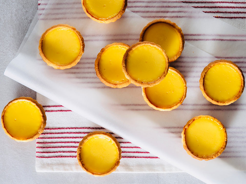 Several egg tarts on a white surface with striped napkins