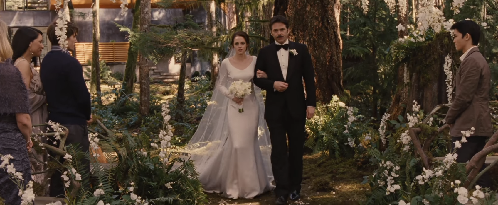 Bella Swan in a wedding dress walks down the aisle with Charlie Swan in a scene from Twilight