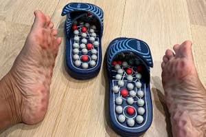 A pair of acupressure slippers placed next to a person's feet on a wooden floor, used for therapeutic purposes