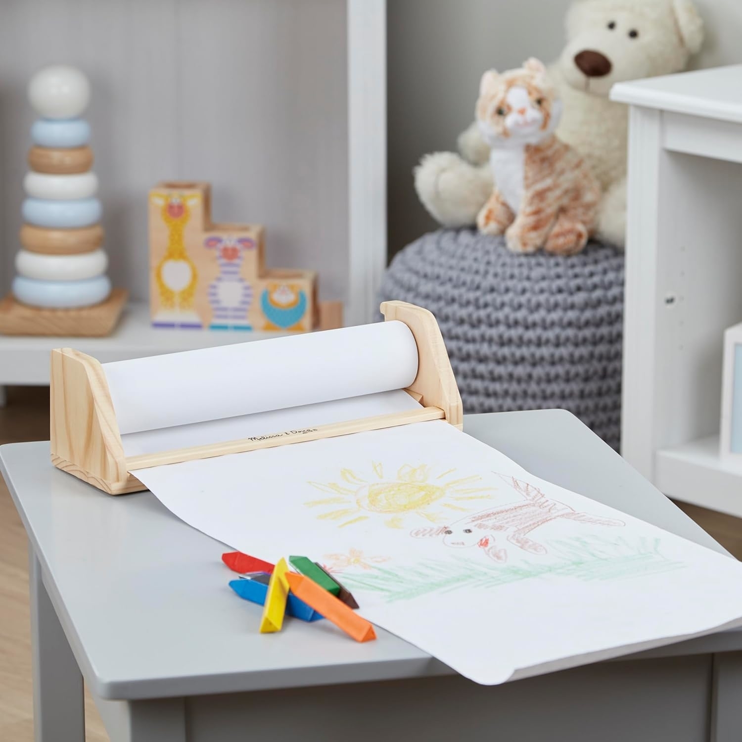 Children's drawing table with paper roll, crayons, and toys in the background
