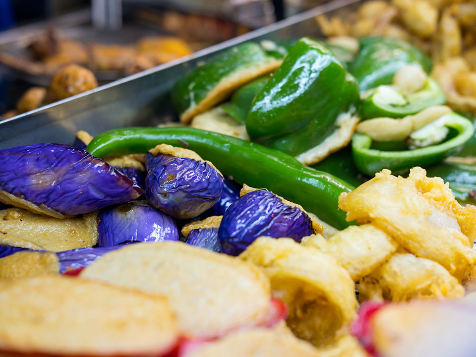 Assorted grilled vegetables including peppers and eggplants displayed at a food market
