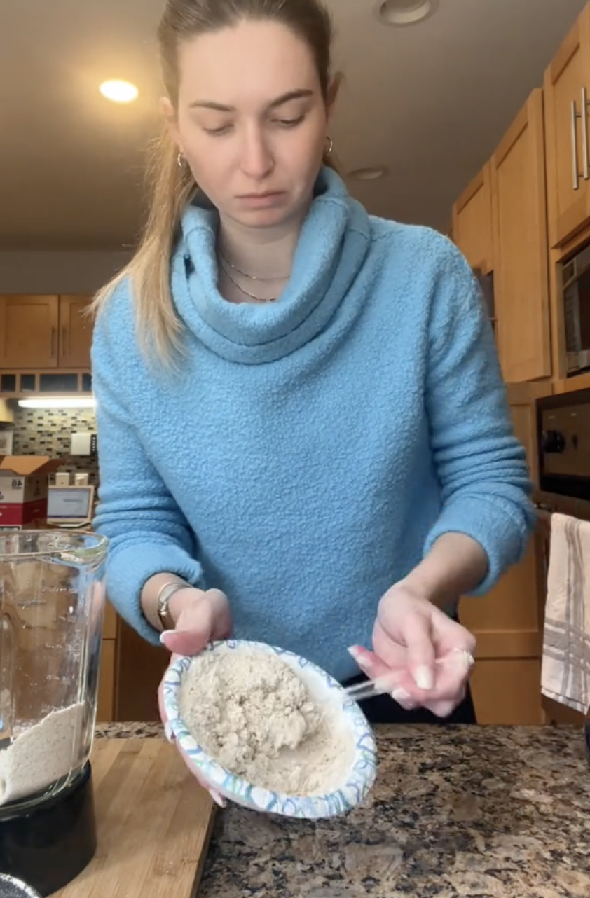 Person in a kitchen scooping flour into a measuring cup for baking