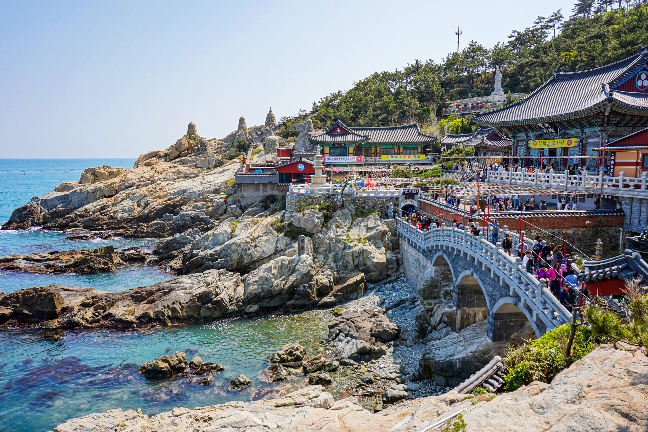 Traditional Korean temple by the sea with a bridge and visitors