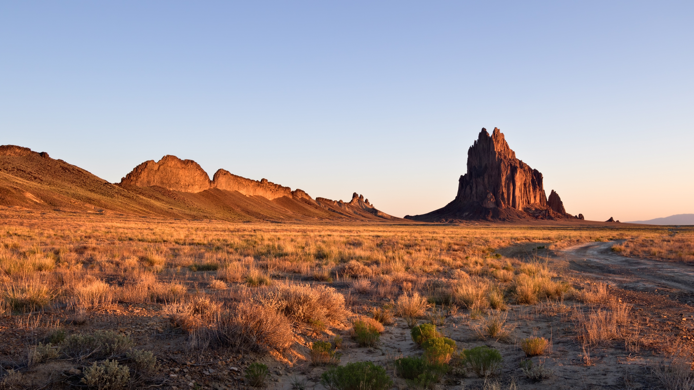 Desert landscape with prominent rock formations and a dirt road under a clear sky at dusk