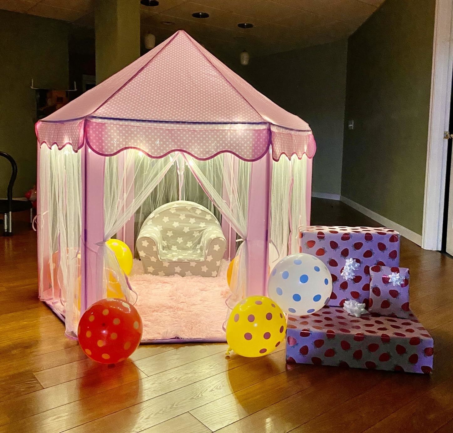 Child's play tent set up indoors with patterned pillows and colorful balloons around it