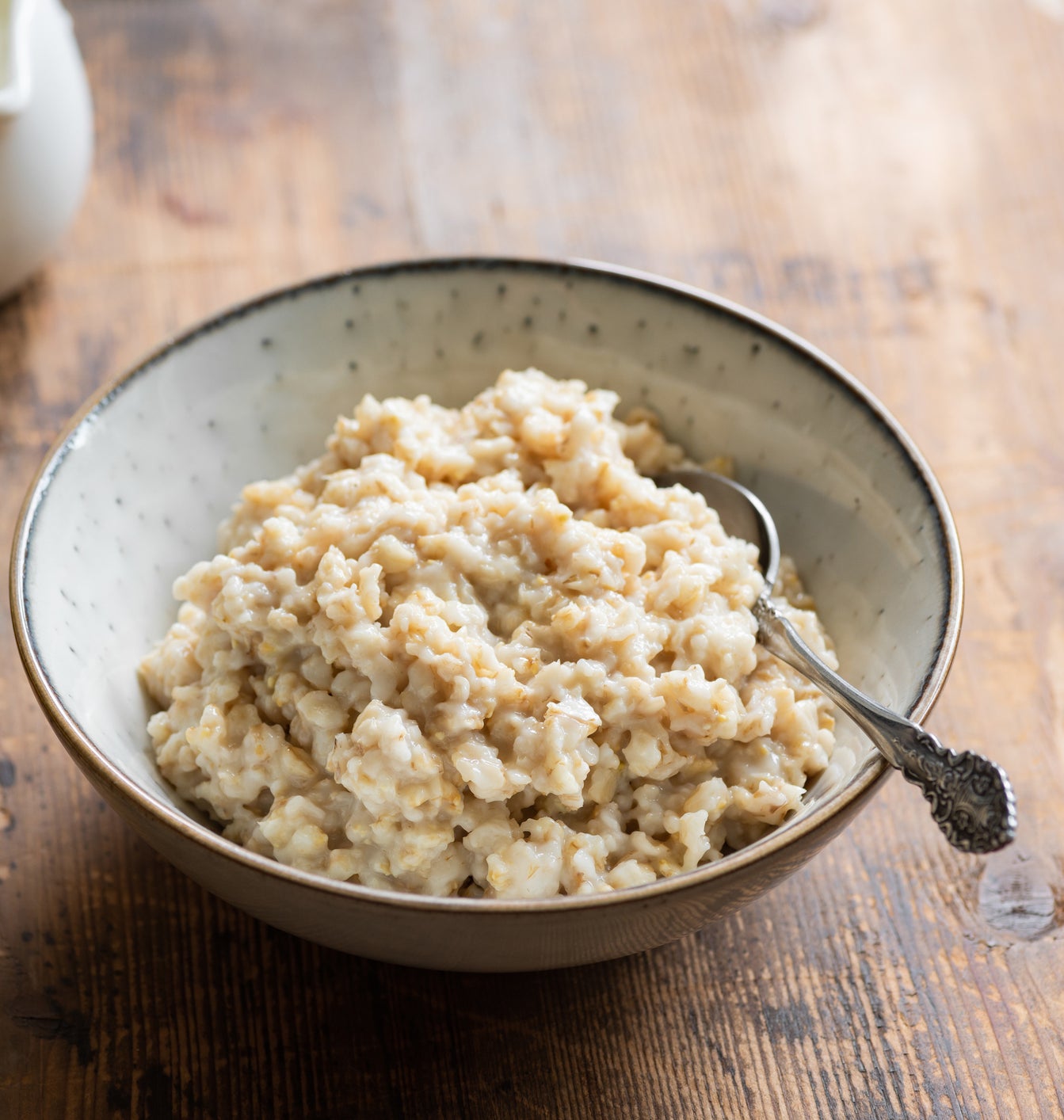 Bowl of oatmeal with a spoon, accompanied by bananas and almonds on a wooden surface