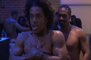 Darryl is shirtless in a scene standing in front of a shirtless man with braids, exhibiting surprise