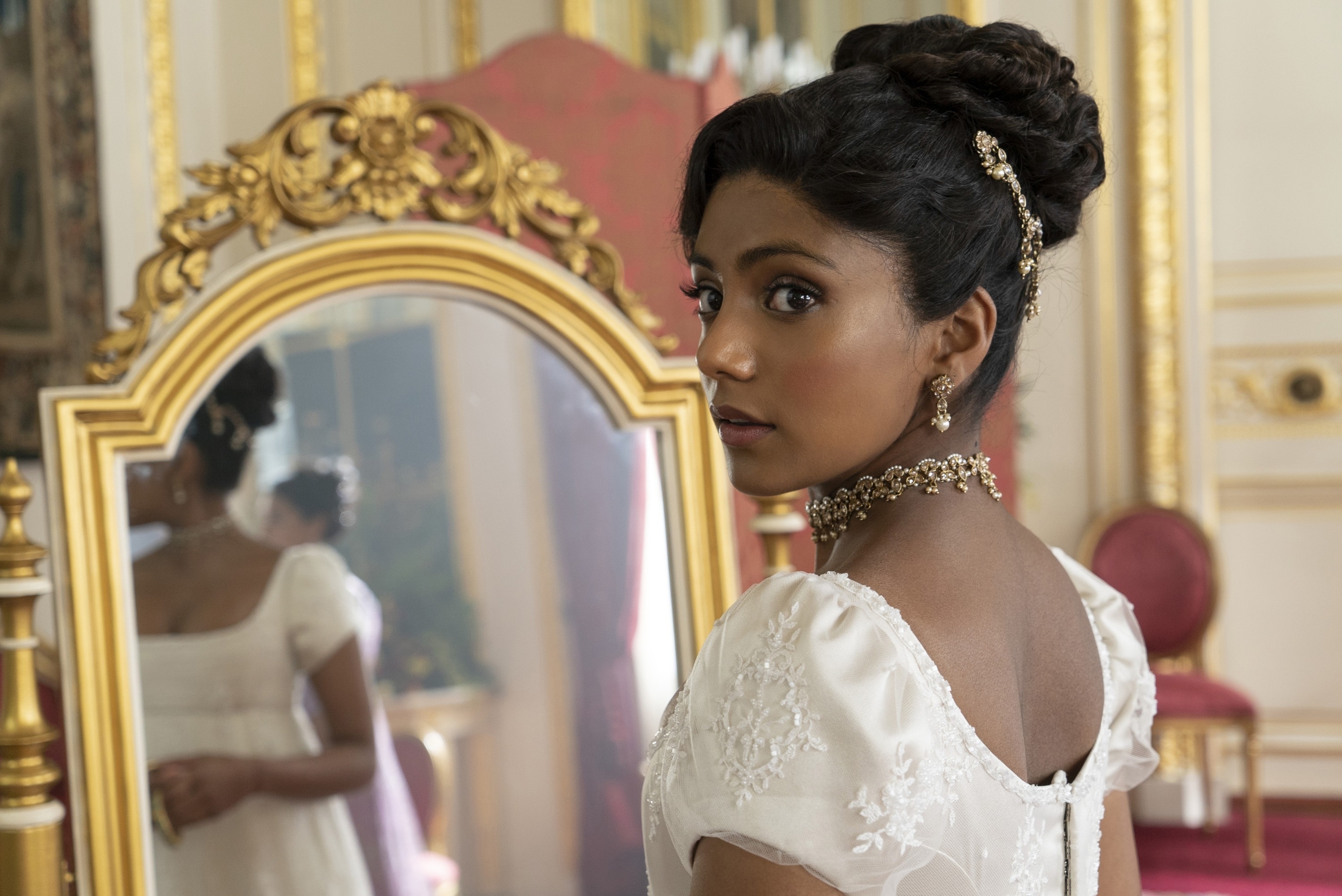 Character in a period drama attire glancing at a mirror, with ornate details and an elegant updo hairstyle
