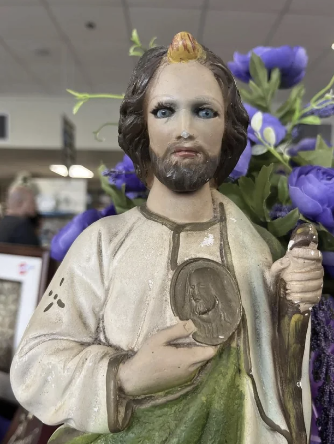 Religious figurine with an oddly painted face displayed among flowers
