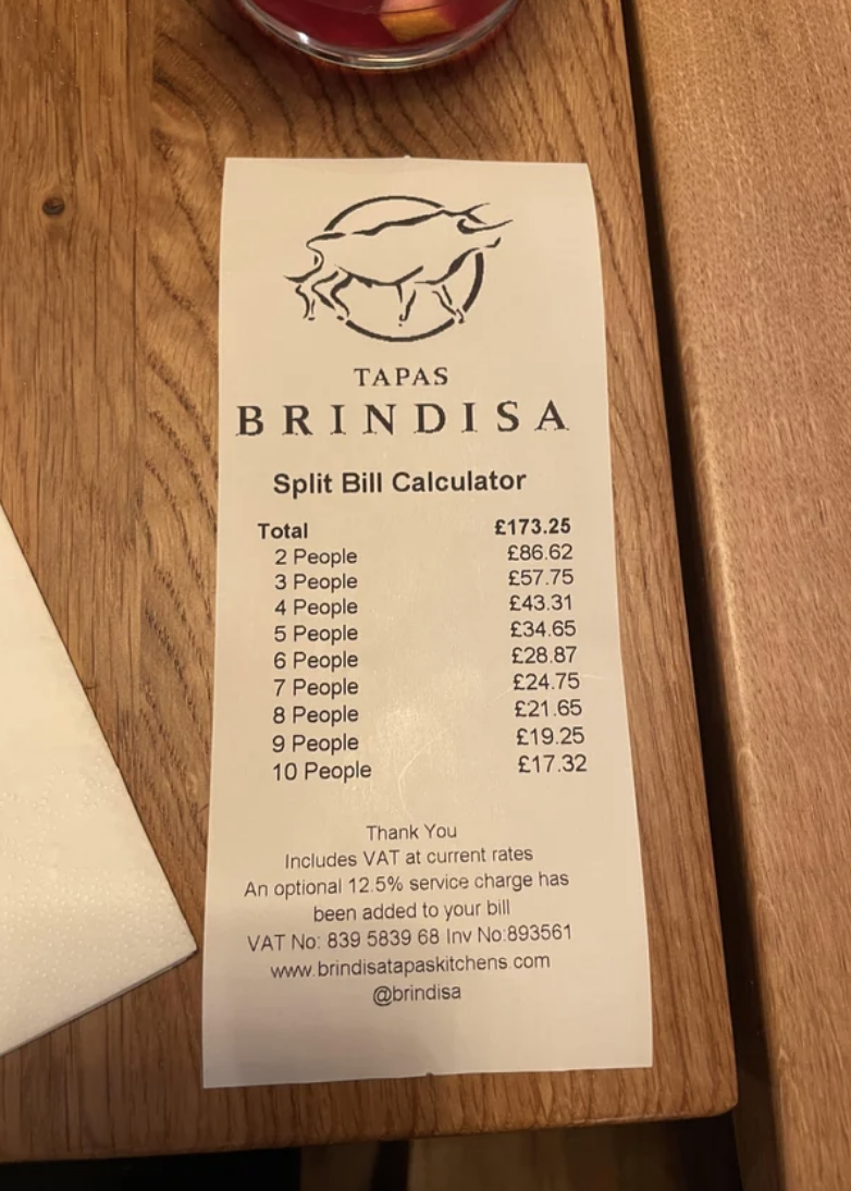 A tapas bill with a split bill calculator for different group sizes, on a wooden table