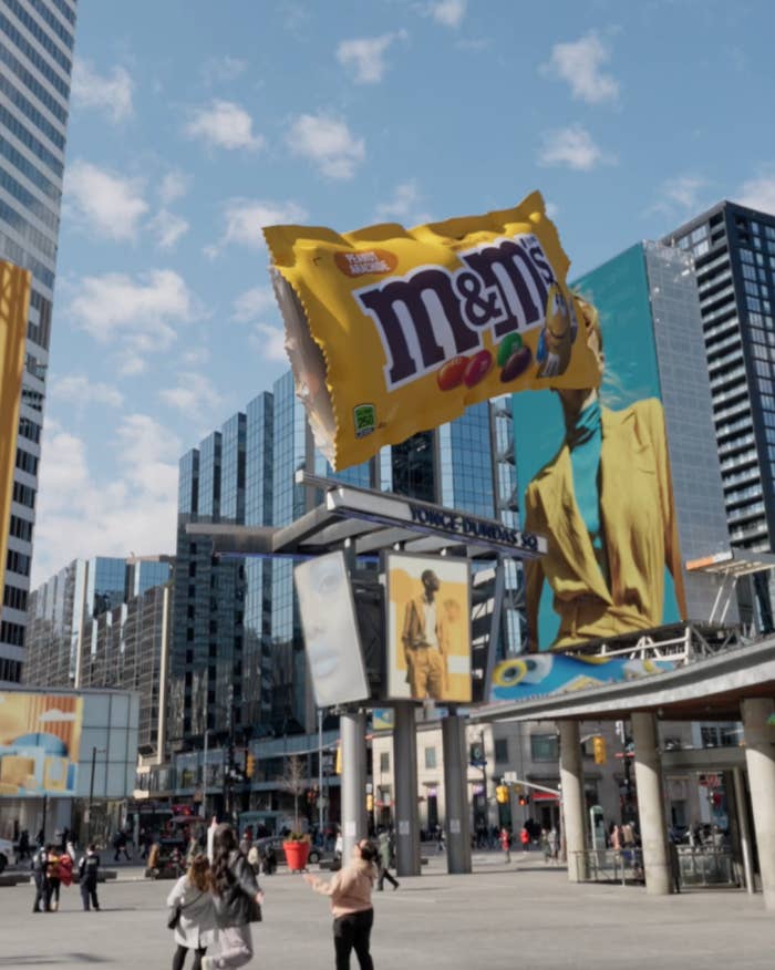 A giant billboard advertisement for M&amp;amp;Ms featuring the yellow M&amp;amp;M character in a city setting