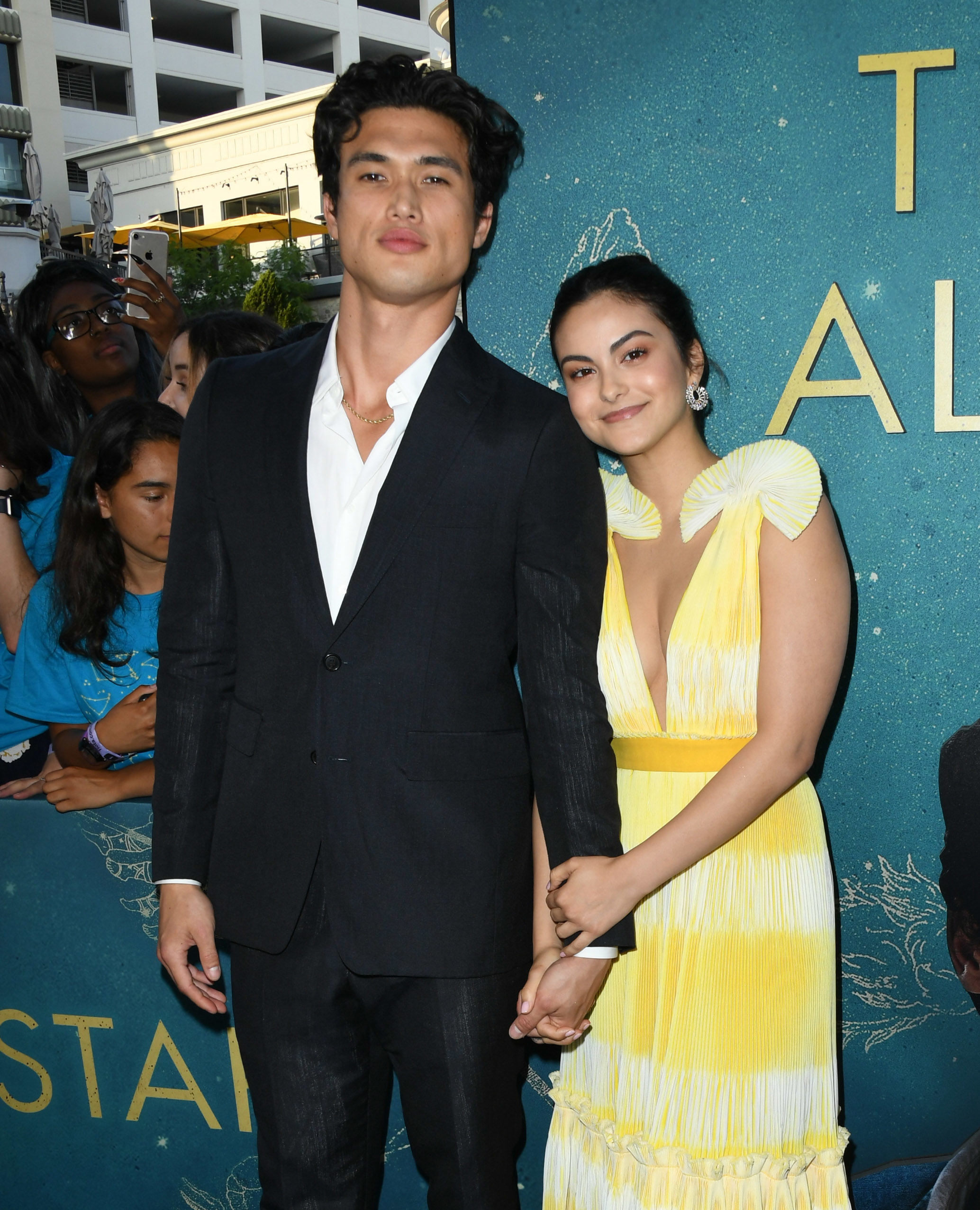 Charles in a suit and Camila in a yellow ruffled dress, holding hands