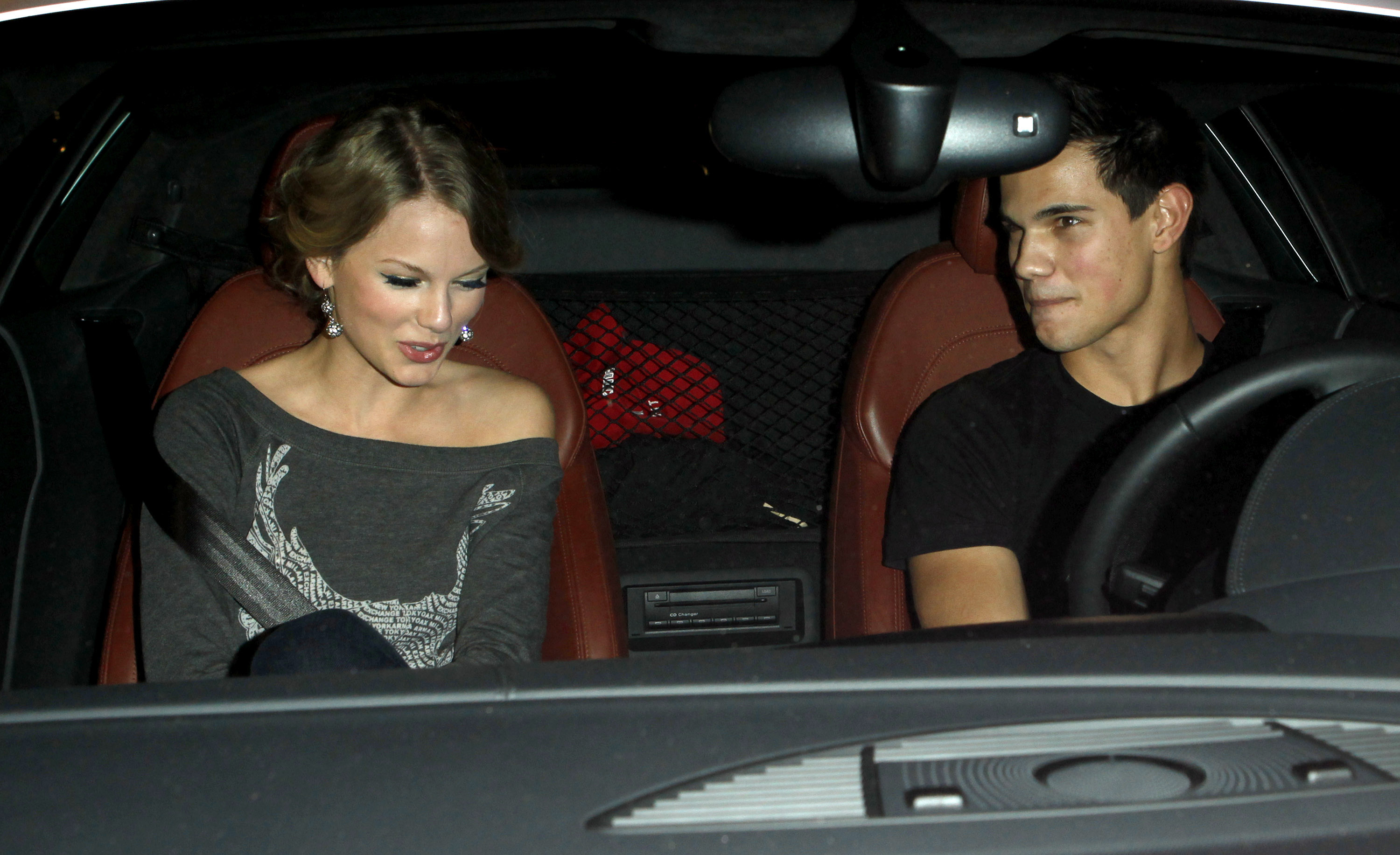 The two Taylors sitting in a car, with he in the driver&#x27;s seat and she in the passenger seat