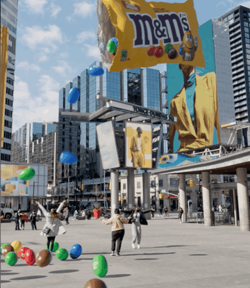 Billboard of M&M's in a city square with oversized candy decorations and people walking
