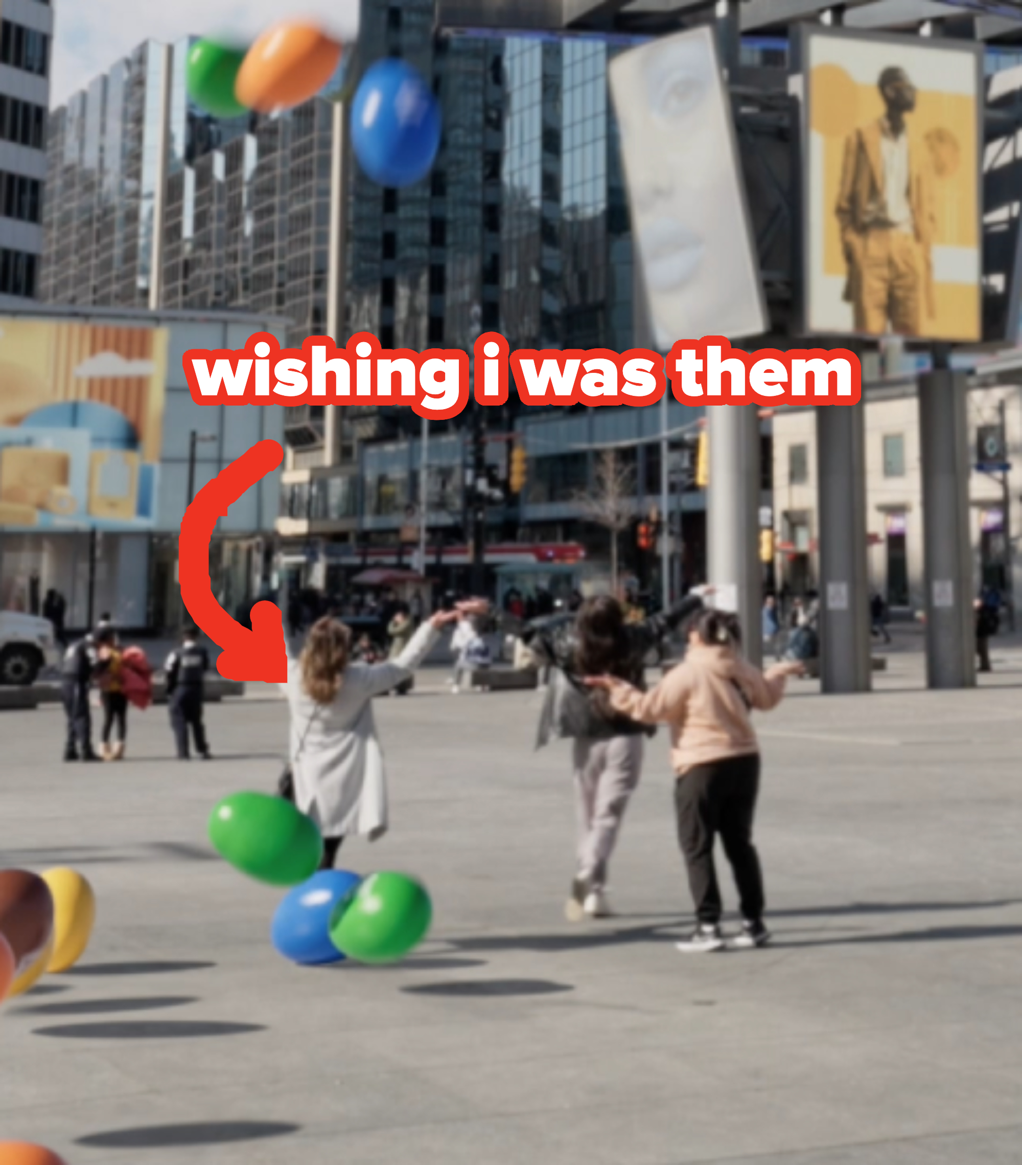 Text overlay says &quot;wishing i was them&quot; above a scene of people with giant M&amp;amp;M&#x27;S at a city square
